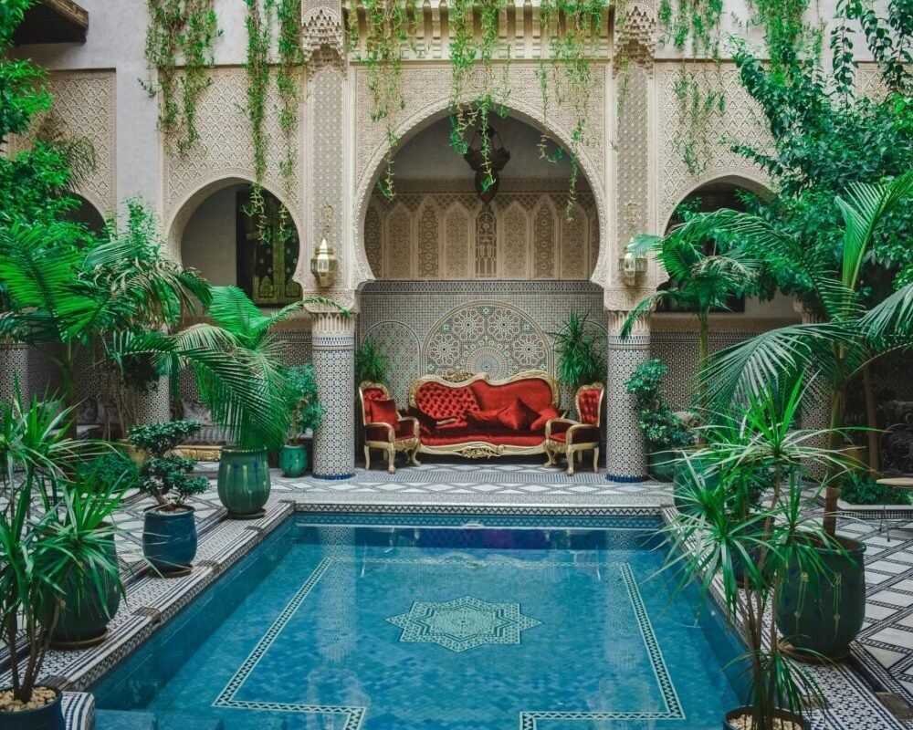 Elegant Moroccan courtyard featuring lush greenery and a decorative pool, perfect for a serene escape.
