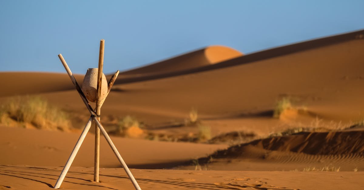 Peaceful desert landscape at Merzouga with sand dunes and wooden tripod under clear blue sky.