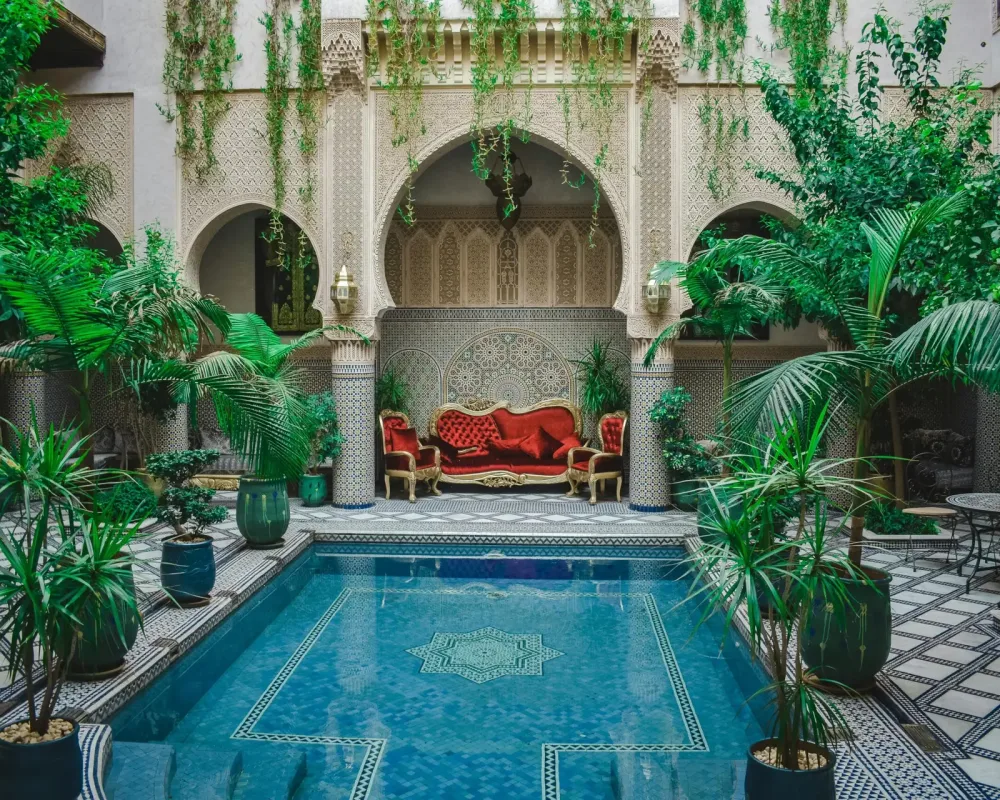 Elegant Moroccan courtyard featuring lush greenery and a decorative pool, perfect for a serene escape.